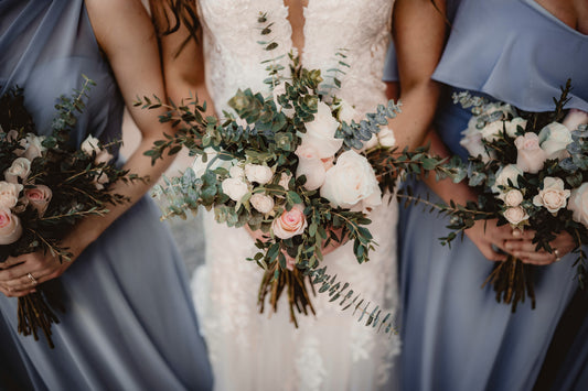 Bride in a white dress holding a bouquet with two bridesmaids in blue dresses holding bouquets.