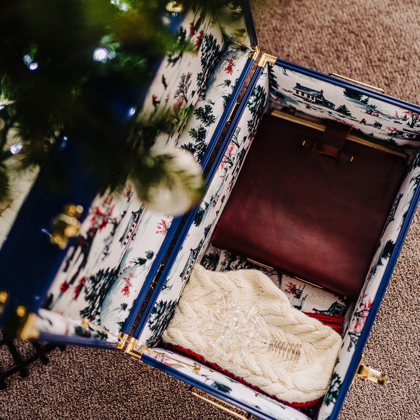 Open trunk with patterned exterior containing a white cable-knit sweater, next to a Christmas tree.