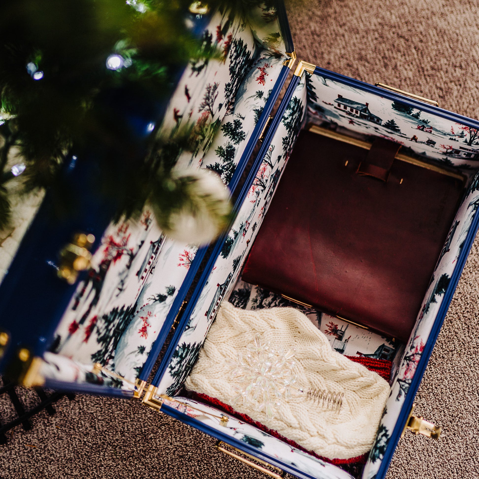 Open trunk with patterned exterior containing a white cable-knit sweater, next to a Christmas tree.