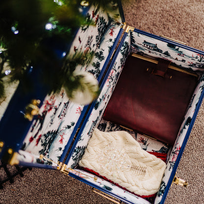 Open trunk with patterned exterior containing a white cable-knit sweater, next to a Christmas tree.