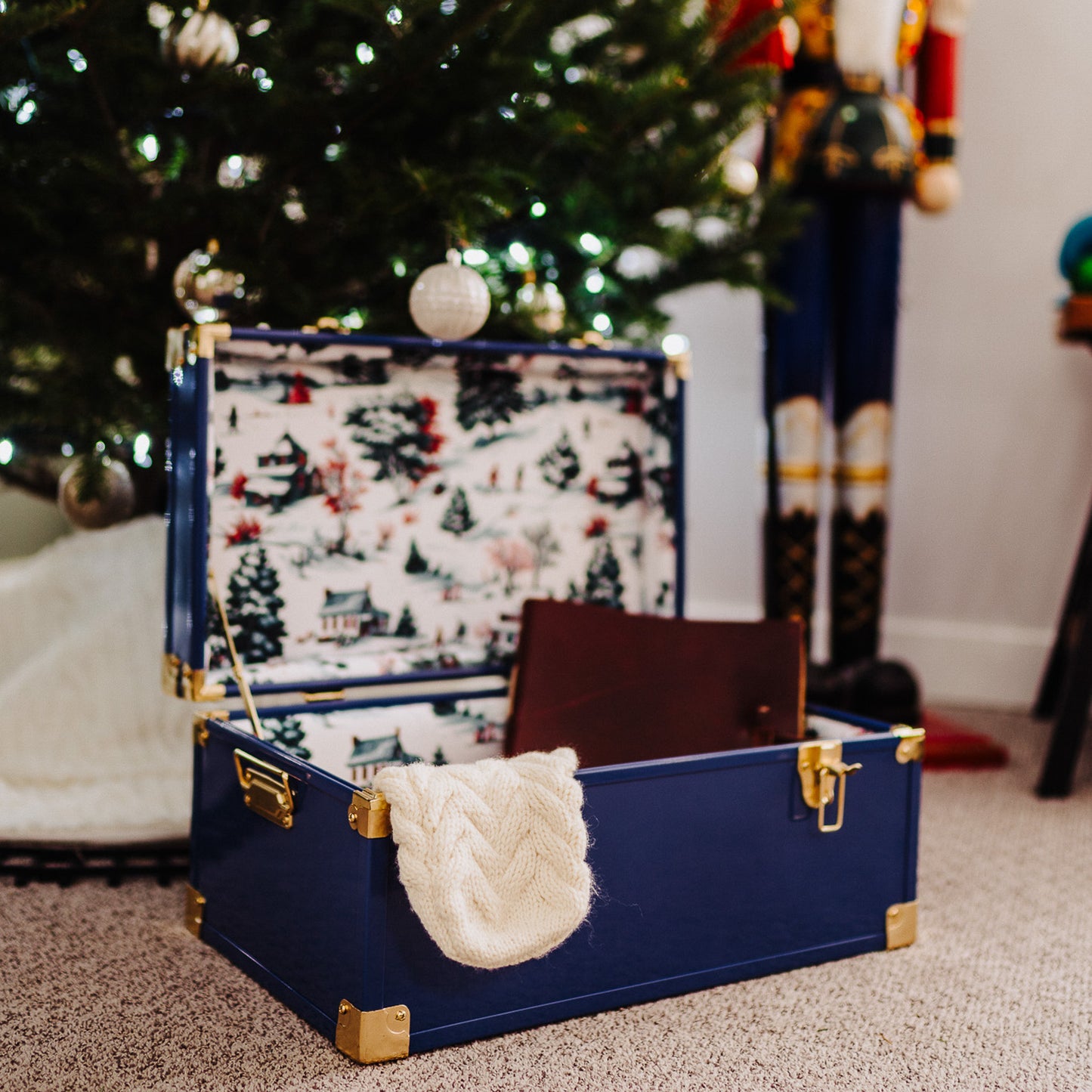 Navy trunk with Christmas-themed interior and decorations in front of a Christmas tree.