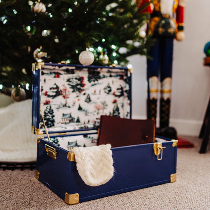 Navy trunk with Christmas-themed interior and decorations in front of a Christmas tree.