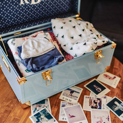 Open blue trunk with baby clothes and photos on a wooden floor