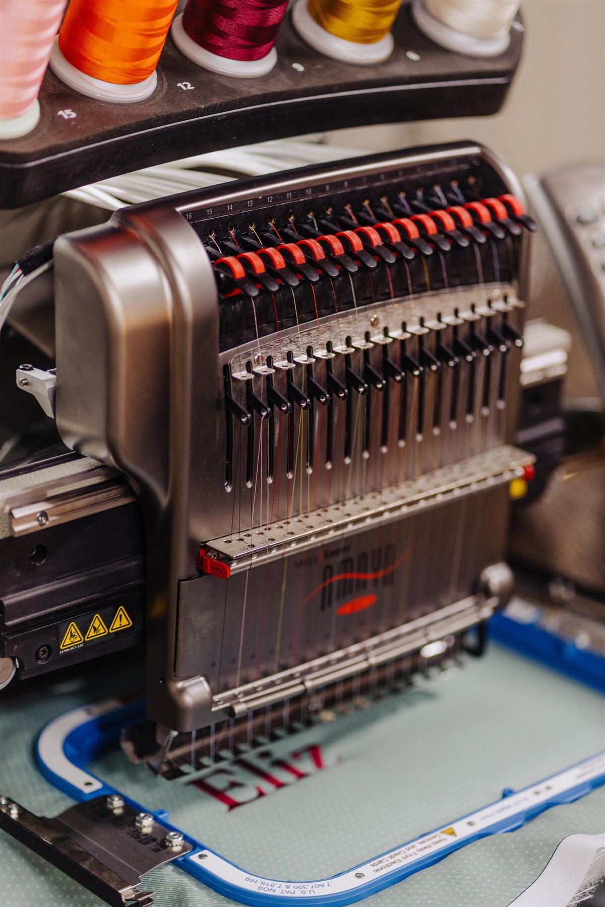 Multi-needle embroidery machine with colorful thread spools stitching a name into a Momento trunk lining