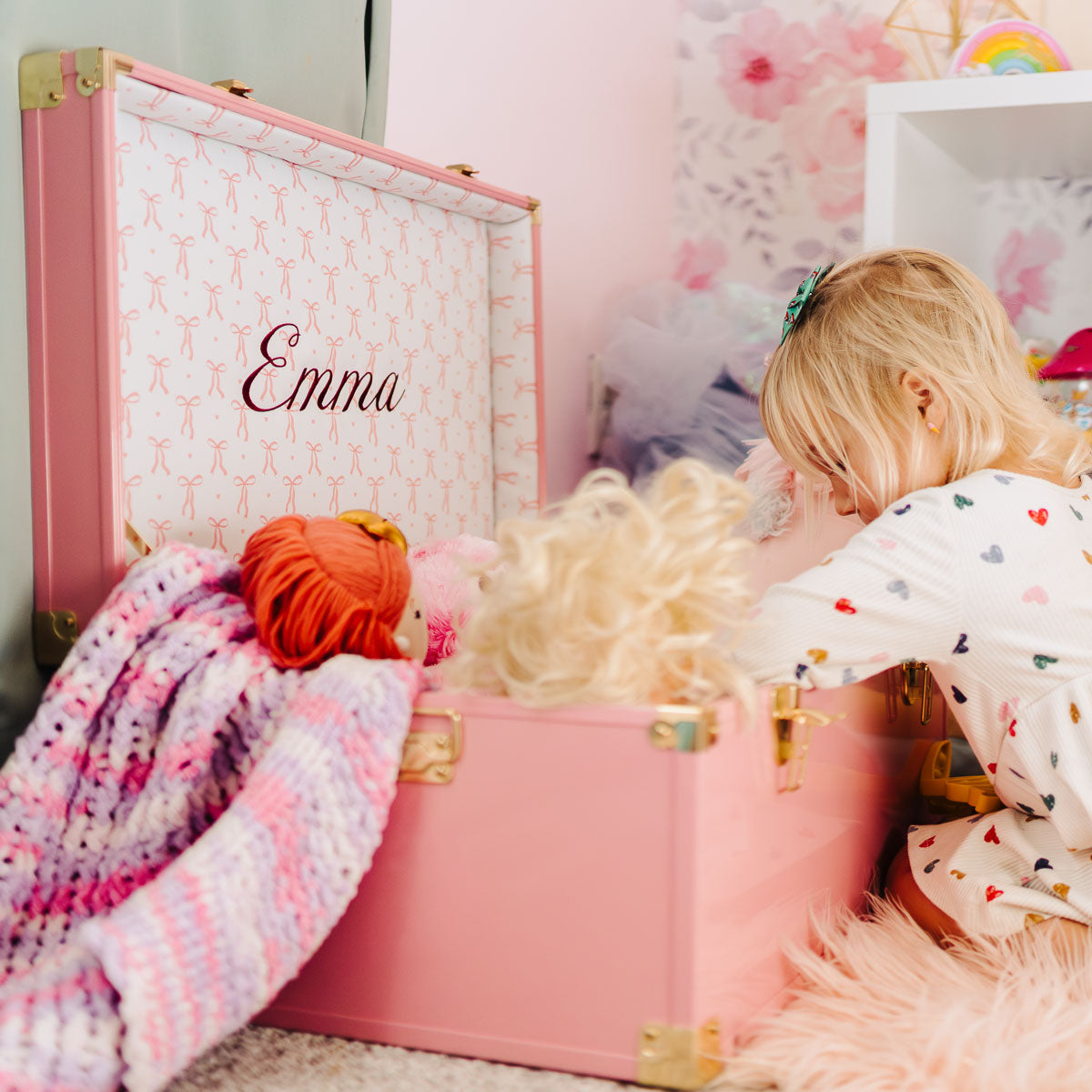 Child playing with pink trunk filled with toys in a room.
