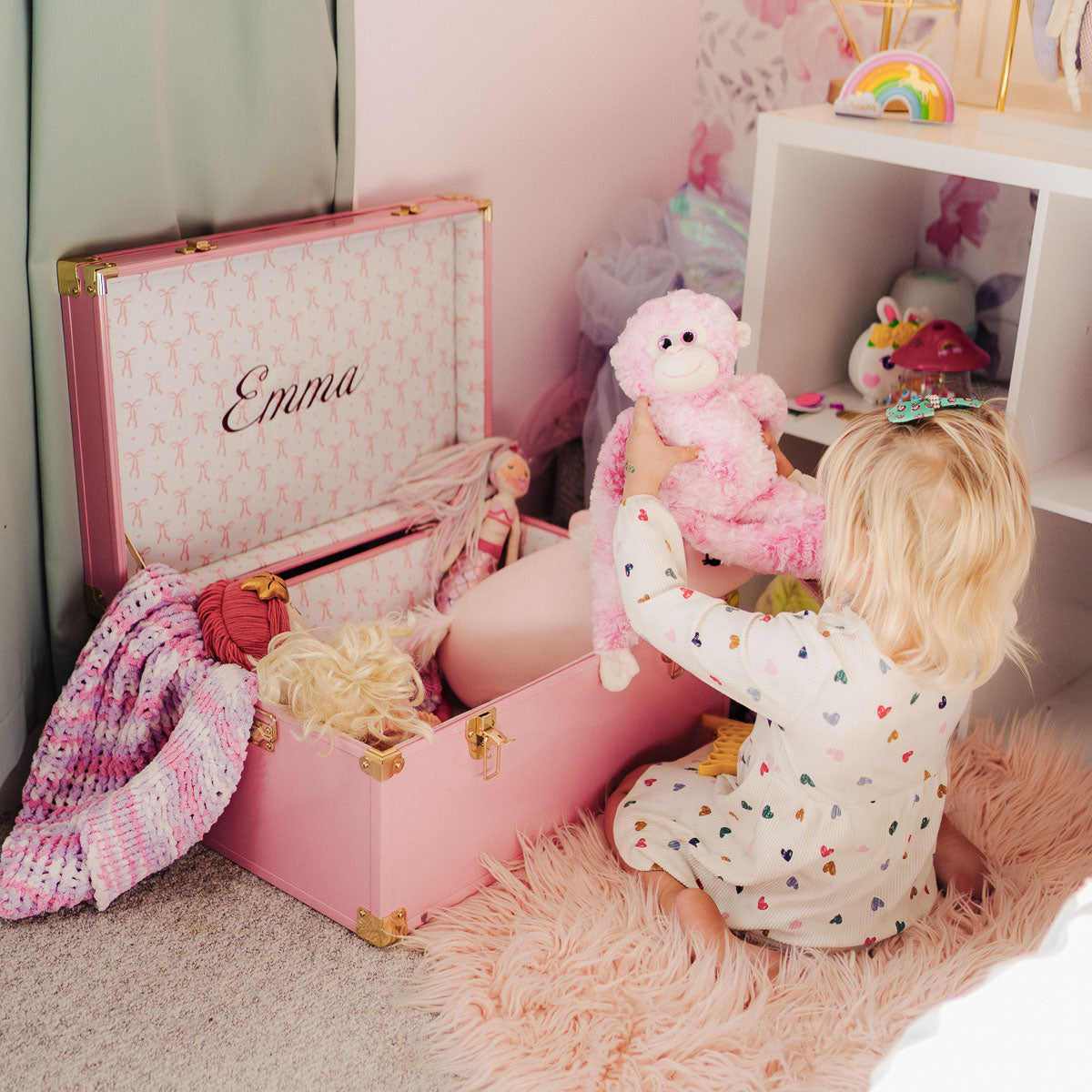 Child playing with a pink trunk labeled 'Emma' filled with toys.