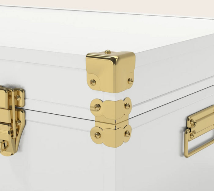 Close-up of a white hard case with polished gold metal corner protectors and latch hardware, shown against a clean white background.